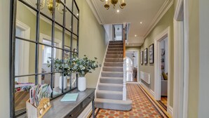 A hallway with a patterned floor, a staircase, and a mirror with a plant.