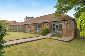 Une maison de plain-pied en briques, avec un toit en tuiles, une porte d’entrée et un petit jardin devant, agrémenté d’un chemin de gravier.