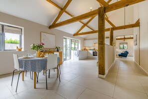 Une cuisine spacieuse avec des poutres en bois, un coin repas avec une table dressée pour quatre personnes, et un canapé bleu dans l’espace salon.