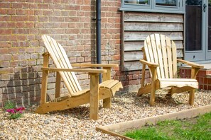 Deux fauteuils Adirondack en bois, placés sur du gravier, avec un mur de briques et un bardage en bois en arrière-plan.