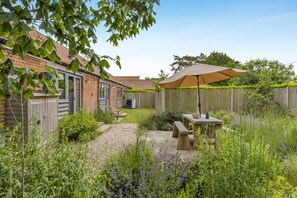 Un jardin avec une terrasse, une clôture en bois et un potager.