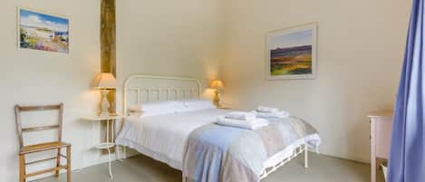 A bedroom with a bed, two bedside lamps, a chair, and two paintings on the wall.