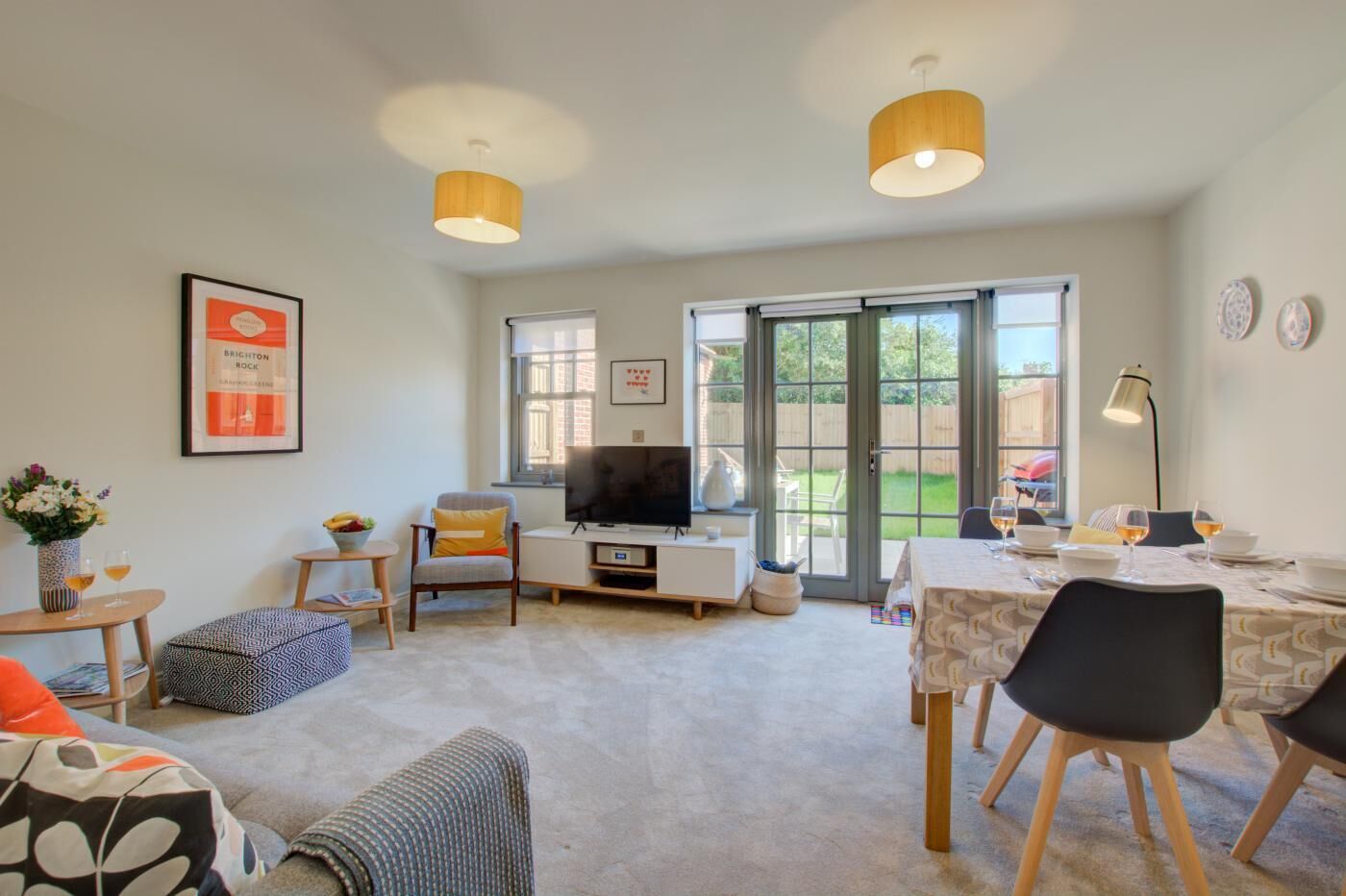 A modern living room with a TV, seating, and a dining area with a table set for two.