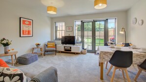 A modern living room with a TV, seating, and a dining area with a table set for two. - 2 Bed in Mundesley (oc-1991) (Mundesley)