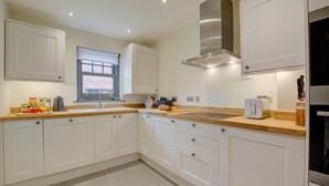 A modern kitchen with white cabinets, a stainless steel range hood, a window, and a toaster. - 2 Bed in Mundesley (oc-1991) (Mundesley)