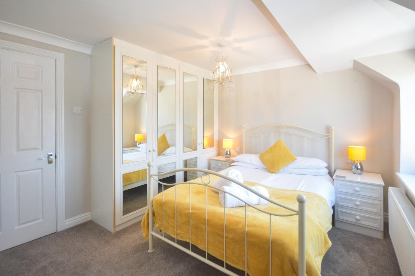 A bedroom with a bed, a wardrobe with mirrors, bedside lamps, and a chandelier.