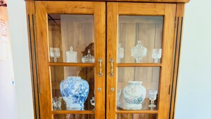 Ein Holzschrank mit Glastüren und Schubladen, gefüllt mit verschiedenen Gläsern und Dekorationsobjekten.