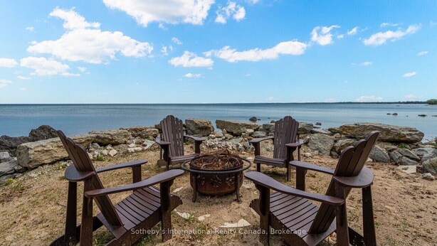 Et siddeområde ved stranden med Adirondack-stole og en bålplads, med udsigt over et roligt hav og en stenet kystlinje.