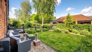 Eine Terrasse mit Korbmöbeln und einer kleinen Feuerstelle, umgeben von einem gepflegten Rasen und Garten.
