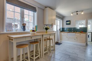 A kitchen with a central island, bar stools, a window with a view, and a tiled backsplash. - 4 Bed in Mundesley (oc-1997) (Mundesley)