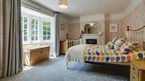 A bedroom with a bed, a dresser, a chest of drawers, a window with curtains, a fireplace, and a mirror on the wall. - 4 Bed in Mundesley (oc-1997) (Mundesley)
