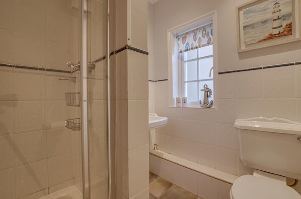 Une salle de bain avec une douche à parois de verre, une fenêtre donnant sur la mer et des toilettes blanches.