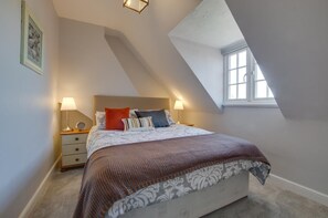 A bedroom with a sloped ceiling, a bed with patterned bedding, a bedside table with a lamp, and a window providing natural light. - 4 Bed in Mundesley (oc-1997) (Mundesley)