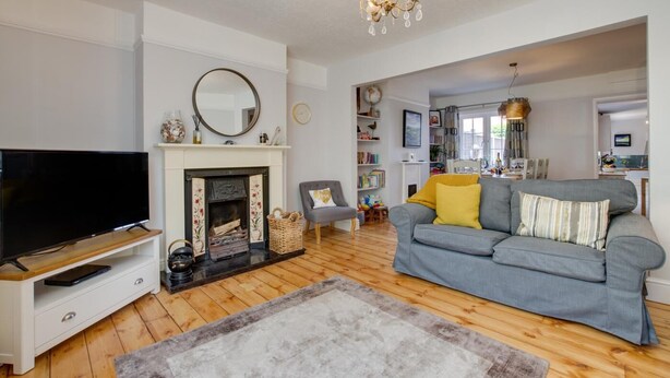 A living room with a fireplace, a television, a grey sofa, and a chandelier. - 4 Bed in Mundesley (oc-1997) (Mundesley)