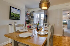 A dining area with a wooden table set for four, a bookshelf, and a window with curtains. - 4 Bed in Mundesley (oc-1997) (Mundesley)