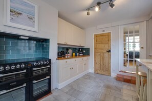 A kitchen with a double oven, white cabinets, a wooden door, and a tiled backsplash. - 4 Bed in Mundesley (oc-1997) (Mundesley)