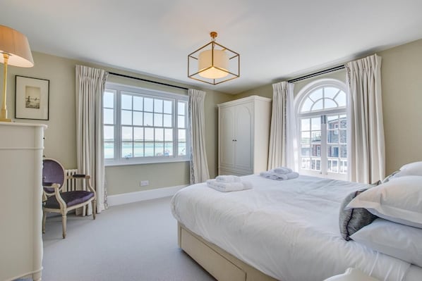 A hotel room with a large bed, a chair, a wardrobe, and a window with a view of the sea. - 6 Bed in Padstow (oc-p00760) (Padstow)