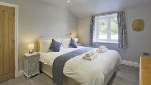 Un dormitorio con cama, mesitas de noche, una ventana con cortinas y una puerta de madera.