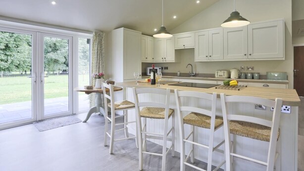 Een moderne keuken met witte kasten, een centraal eiland met barkrukken en een grote schuifpui naar een tuin.