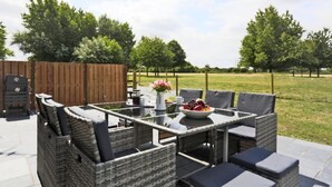 Een terras buiten met rieten meubels, een tafel met een schaal fruit en een barbecue.