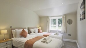 Een hotelkamer met twee bedden, een raam met gordijnen, een nachtkastje met een lamp en een spiegel aan de muur.