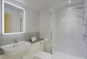 Un baño moderno con un espejo grande, un lavamanos, un inodoro y una ducha con cerramiento de vidrio.