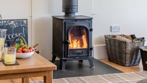 A wood-burning stove with a fire, a table with a bowl of fruit, glasses, and a sign. - 3 Bed in Bassaleg (oc-bow138) (Bassaleg)