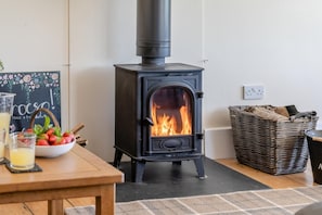 A wood-burning stove with a fire, a table with a bowl of fruit, glasses, and a sign. - 3 Bed in Bassaleg (oc-bow138) (Bassaleg)