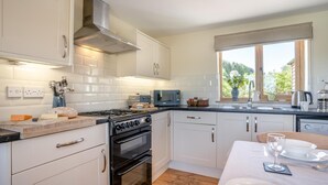 A modern kitchen with white cabinets, a stainless steel range hood, a black oven, and a window with a view of greenery. - 3 Bed in Bassaleg (oc-bow138) (Bassaleg)
