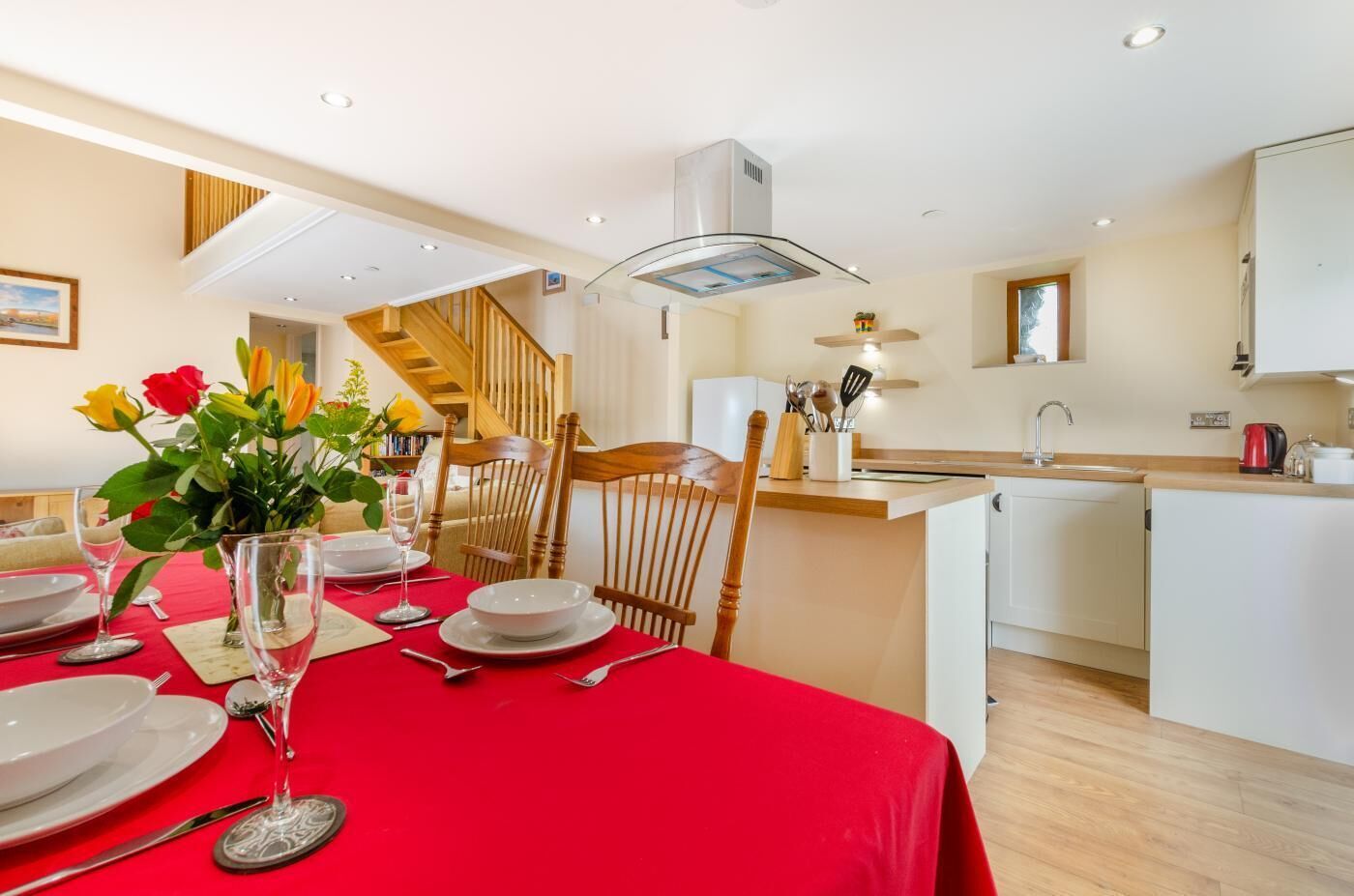 A modern kitchen with white cabinets, a wooden island, and a dining area with a red tablecloth.