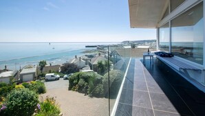 Un balcon offrant une vue dégagée sur la mer, une zone pavée servant de parking et un jardin agrémenté de différentes plantes.