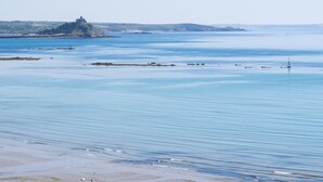 Un paysage côtier avec des eaux calmes, une plage de sable et, au loin, une structure qui ressemble à un château, perchée sur une colline.