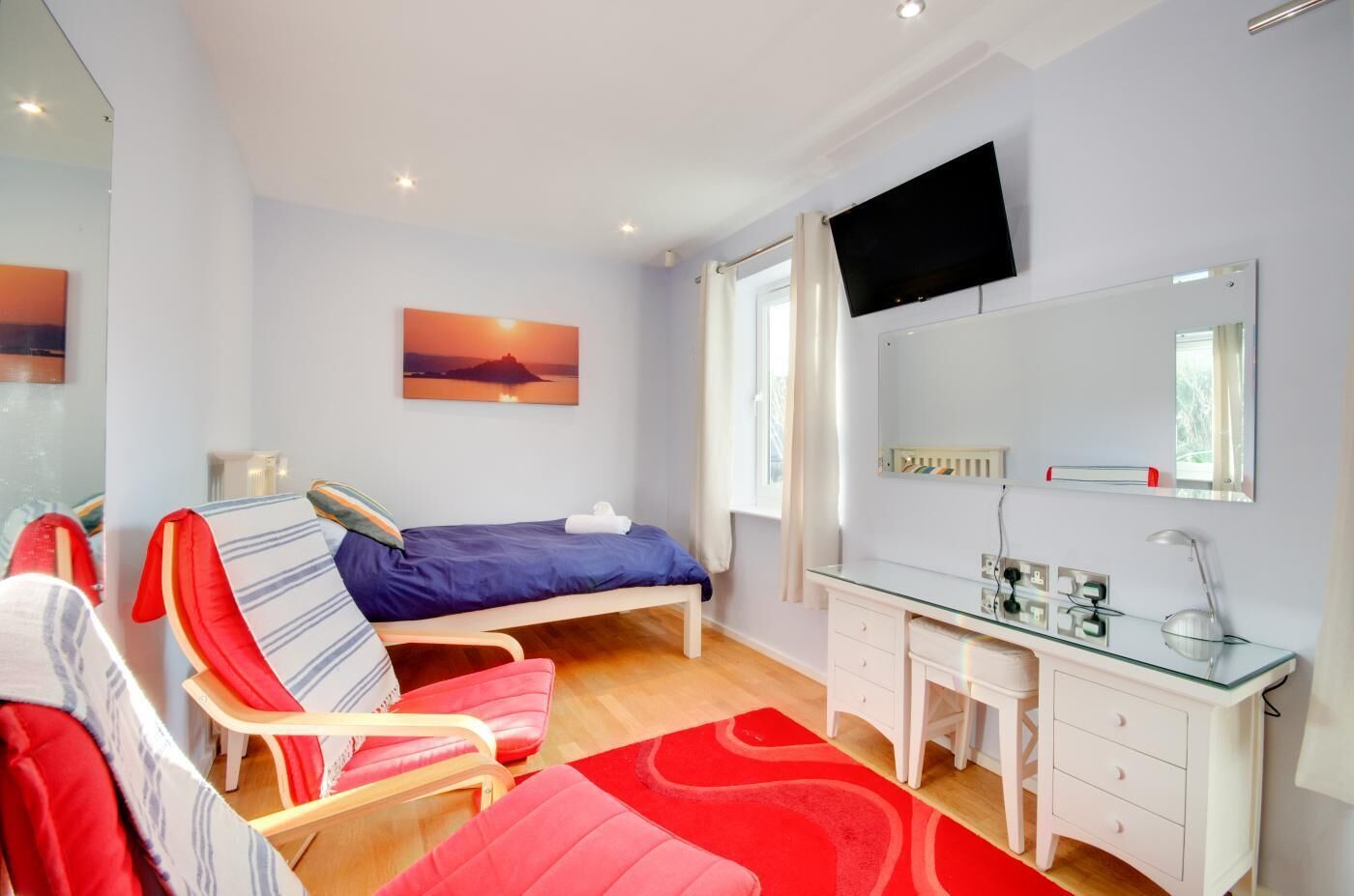 A bedroom with a bed, a desk, a chair, a TV, and a painting.