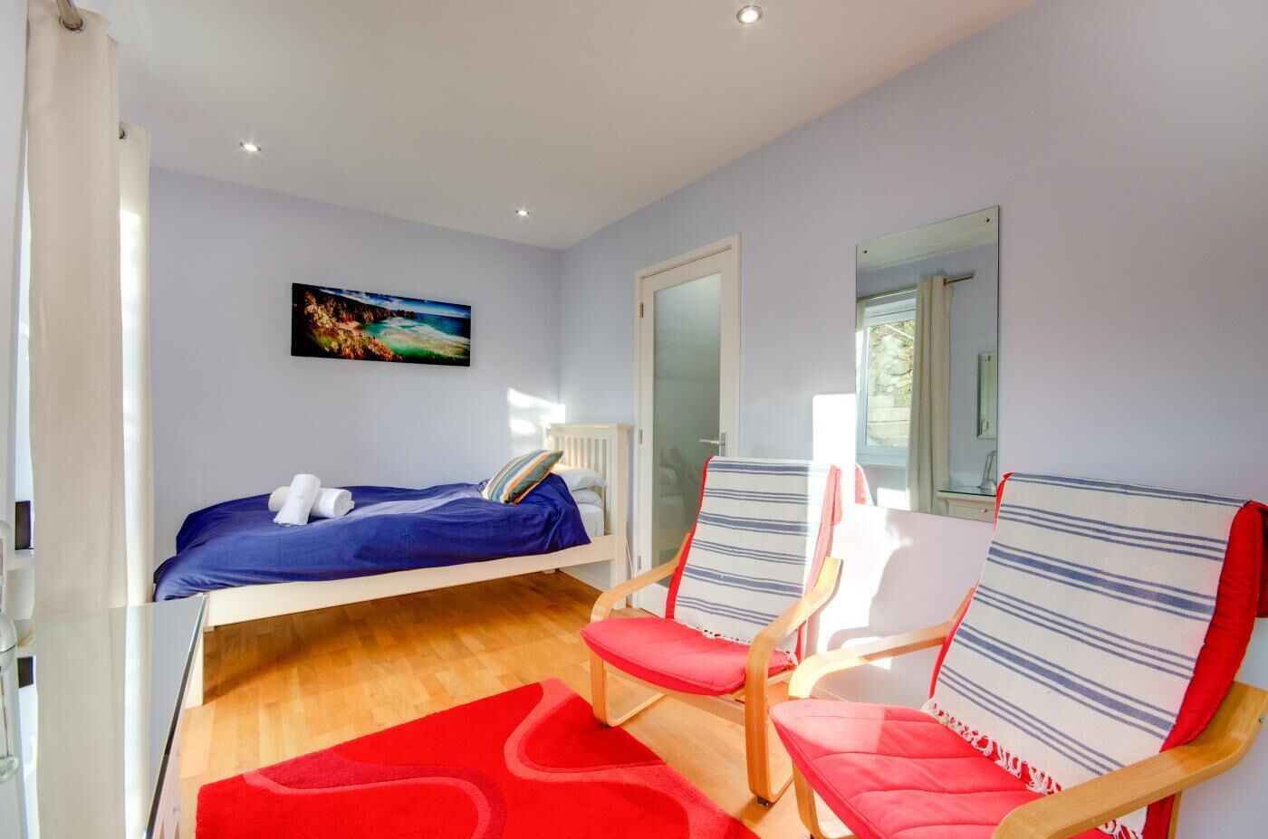 Une chambre à coucher avec un lit, deux chaises, un tapis rouge et un tableau accroché au mur.