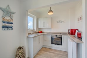 Una cocina compacta con muebles blancos, horno empotrado, lavamanos y ventana.