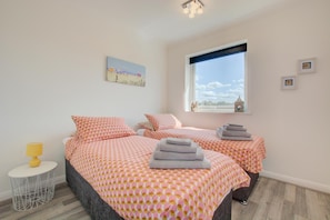 Un dormitorio con dos camas, una mesita redonda con una lámpara, una ventana con vistas, y un cuadro en la pared.