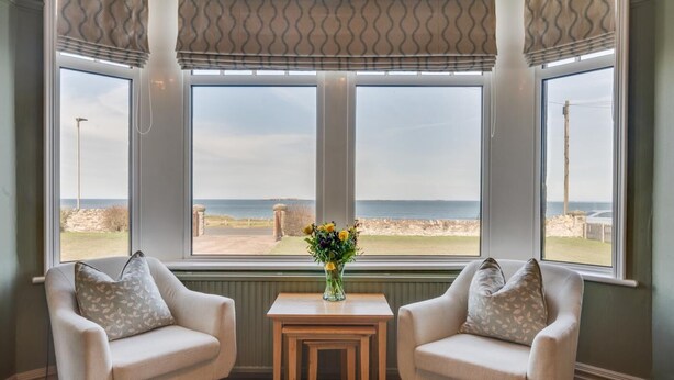 Ein Zimmer mit zwei Sesseln, die zu einem großen Fenster mit Blick auf einen Strand ausgerichtet sind.