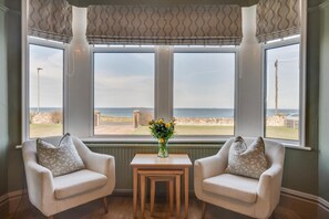 A room with two armchairs facing a large window overlooking a beach. - 5 Bed in Seahouses (oc-88711) (Seahouses)