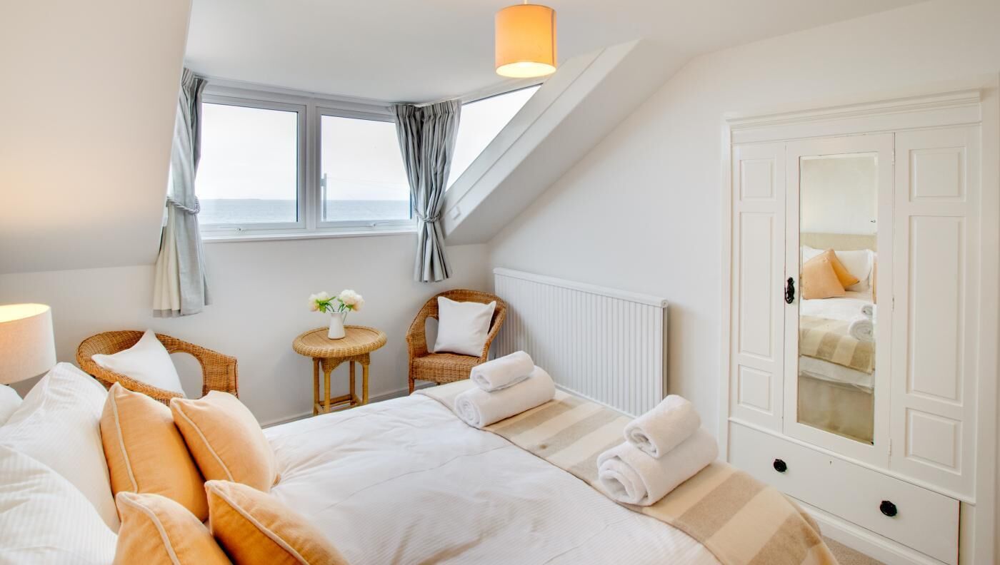 A bedroom with a large bed, a chair, a small table with flowers, and a wardrobe.