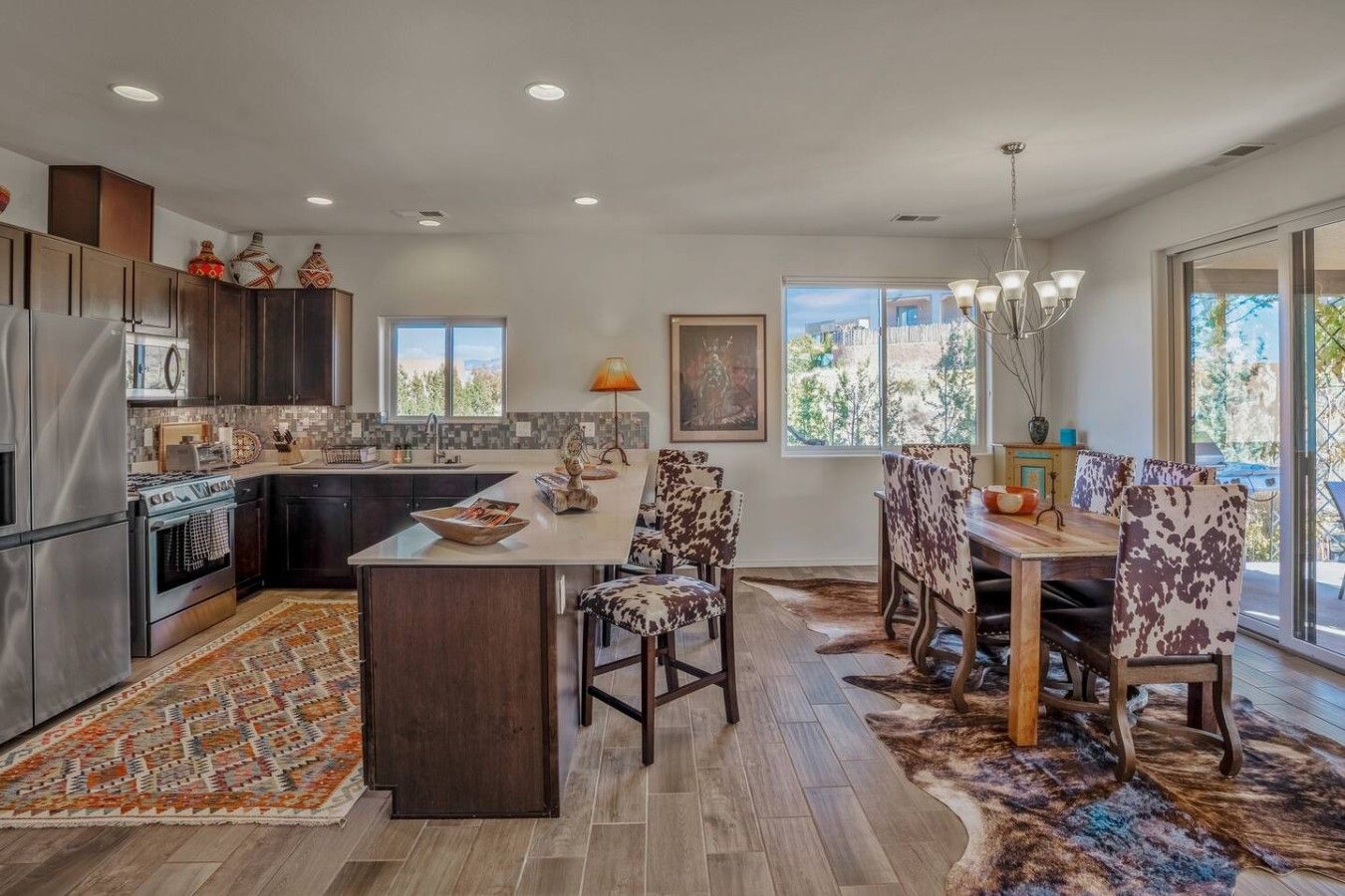 Una cocina moderna con una isla central, muebles oscuros y una zona de comedor con sillas estampadas.