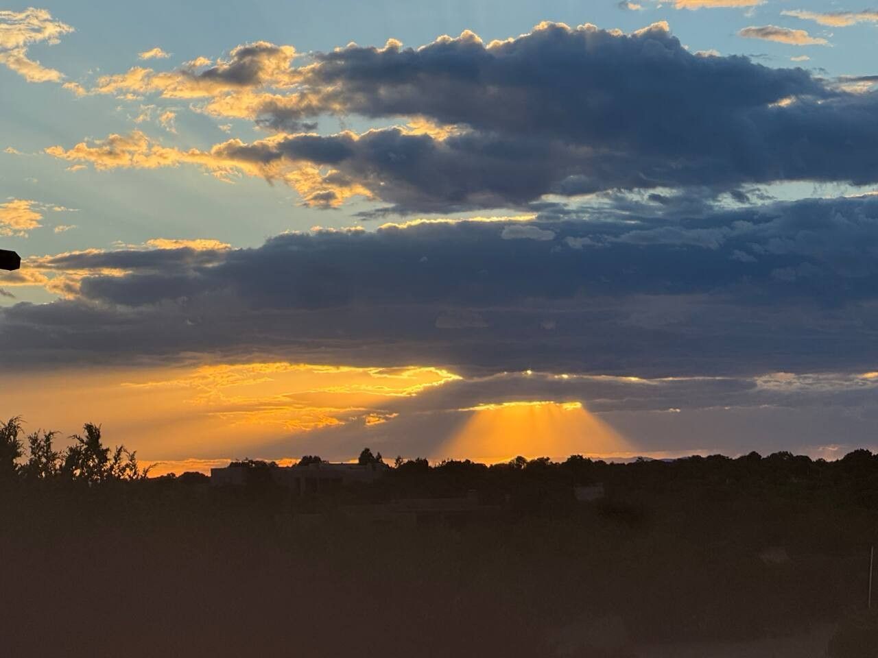 A landscape with a silhouette of trees and buildings against a sunset sky.