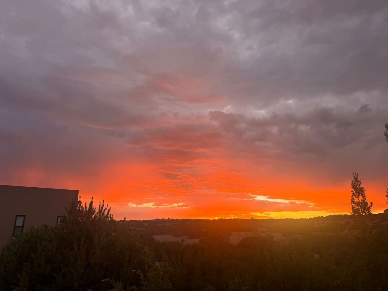 Un coucher de soleil avec la silhouette d’un bâtiment et un arbre au premier plan.