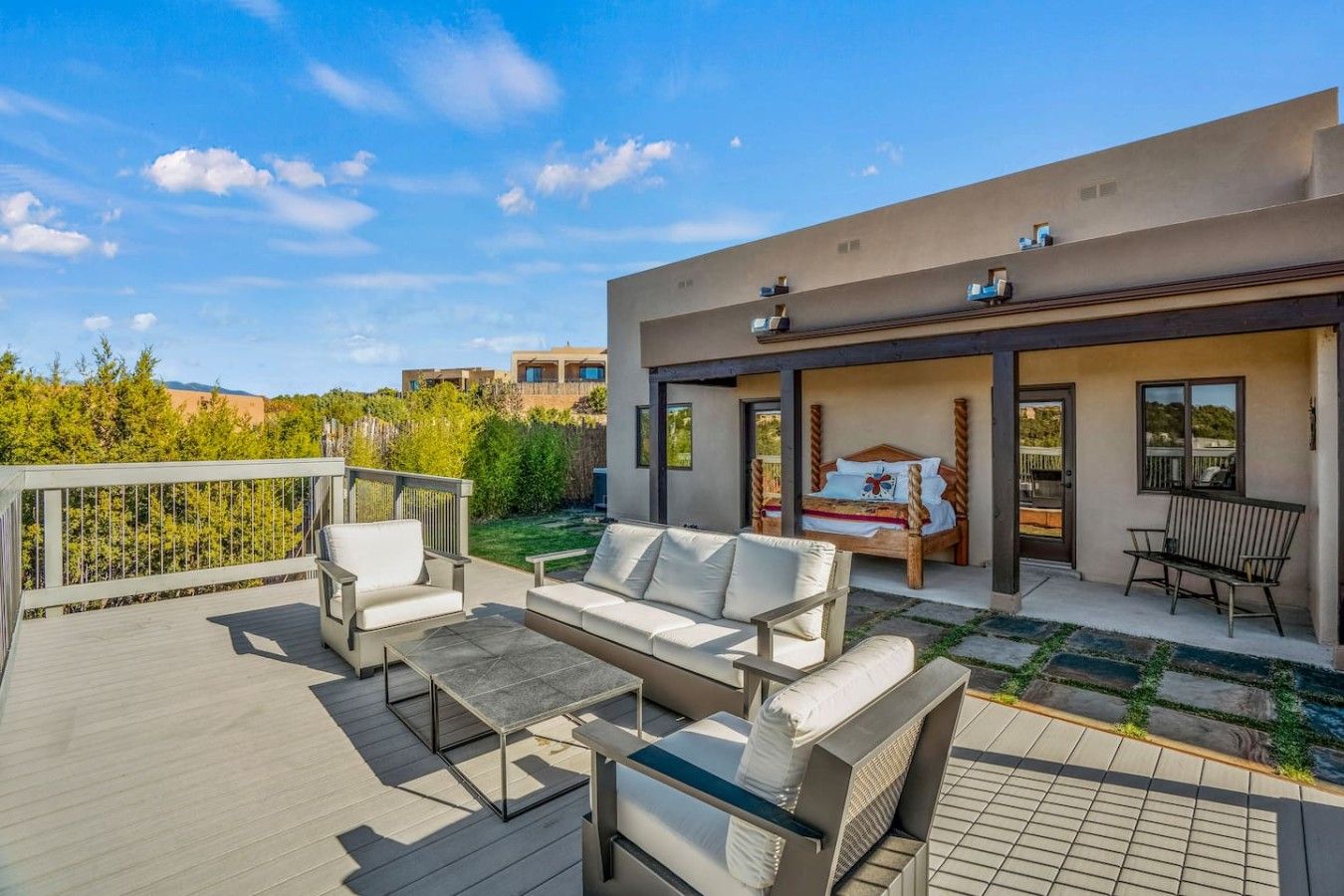 A modern outdoor living area with a deck, seating, and a bedroom with a bed and window.