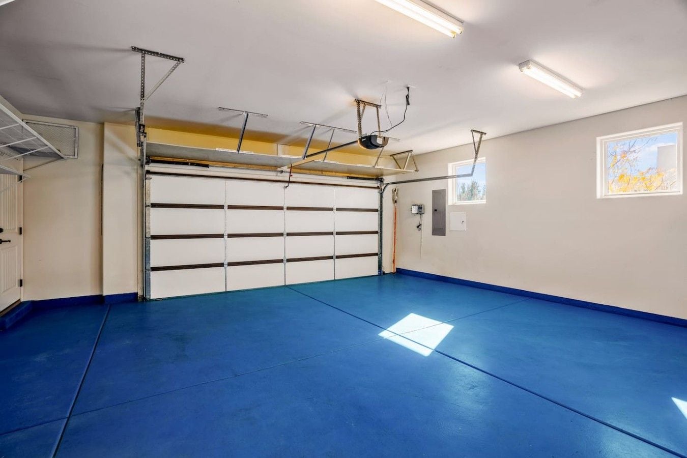 A garage with a blue floor, a white garage door, and overhead lighting.