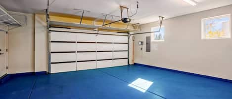A garage with a blue floor, a white garage door, and overhead lighting.