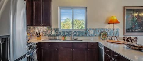 A modern kitchen with dark wood cabinets, a stainless steel refrigerator, a tiled backsplash, and a window with a view of greenery.