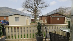 A balcony with a view of a mountain, a wooden deck, a potted plant, and a chair. - Loch Lomond Holiday Home (Arrochar)