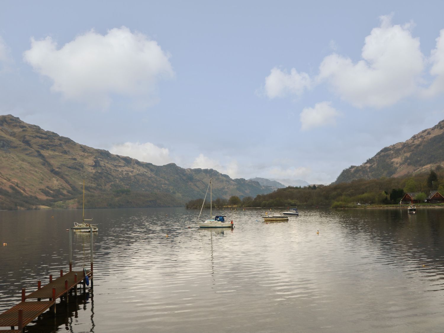 A calm lake with boats, a dock, and mountains in the background.