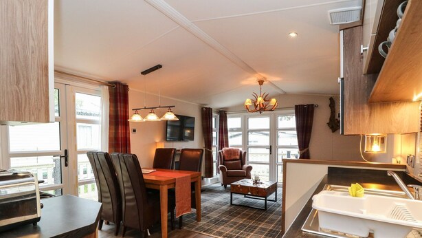 A compact kitchen with a dining area, a small seating space, and a view through large windows. - Loch Lomond Holiday Home (Arrochar)