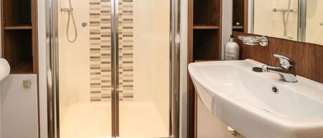 A modern bathroom with a glass-enclosed shower, a white sink with a chrome faucet, and wooden shelving.